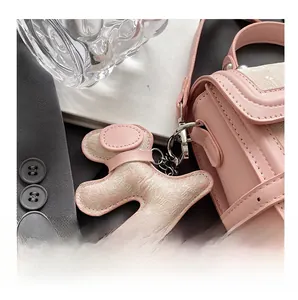 Pink dog-shaped leather charm with silver clasp hanging on a stylish shoulder bag