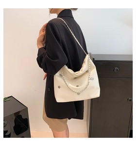 Detail view of large cream tote bag with silver studs and metal chain strap