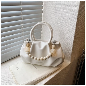 Detail view of cream pleated cloud bag with marble bead chain and top handle