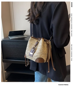 Detail view of woven straw bucket bag featuring dark brown leather trim and metal buckle