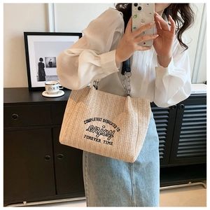 Close-up of beige woven straw tote bag with black embroidery and leather chain strap