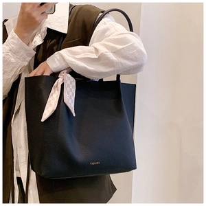 Detail of black pebbled leather tote bag featuring gold letters and checkered scarf ornament