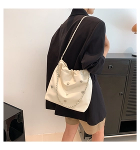 Detail of cream leather shoulder bag featuring heart studs and a silver chain strap