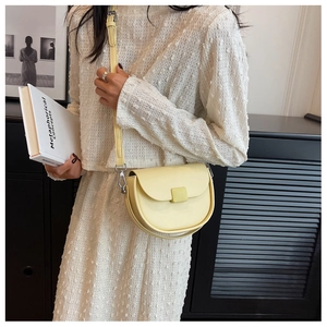 Detail of pale yellow saddle bag with adjustable strap worn by model in white dress