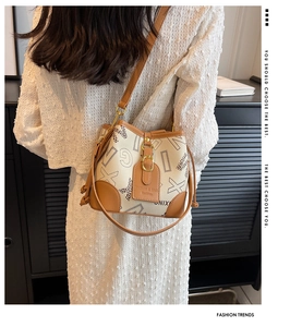 Détail du sac seau crème avec bordure en cuir marron et imprimé monogramme sur modèle