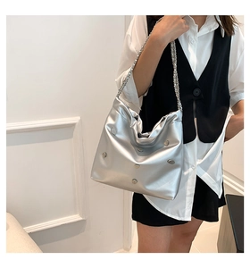 Detail of silver metallic hobo bag featuring heart-shaped rivets and woven chain strap