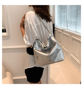 Silver metallic bucket bag with chunky chain strap and heart stud detail shown on model
