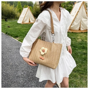 Detailed close-up of woven straw tote with floral crochet ornament and leather chain strap