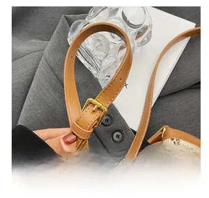 Détail de la bandoulière réglable en cuir marron avec boucle dorée sur un sac seau