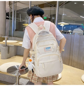 Detail of a cream nylon backpack with side buckle straps and a small duck plush charm