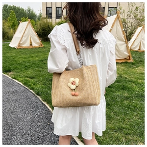 Detail of woven straw tote bag with 3D floral accents and cherry charm in outdoor setting