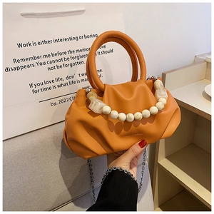 Nahaufnahme der orangefarbenen Cloud-Bag mit weißem Perlengriff und silberner Kette