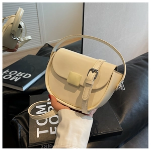 Detail shot of a cream saddle bag featuring textured faux leather and a silver buckle accent