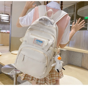 Detail of cream nylon backpack featuring multiple zip pockets and a cute duck plush charm