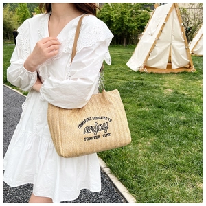 Detail of woven straw tote bag with black embroidery and leather chain strap in outdoor setting