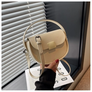 Detail of off-white saddle bag with top handle and adjustable strap in soft light
