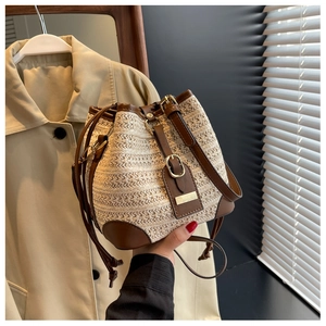Detail of woven straw bucket bag with dark brown leather trim and golden metal hardware