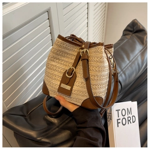 Detail of woven straw bucket bag with dark brown leather trim and metal buckle
