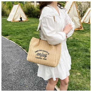 Close-up of beige straw woven tote bag featuring black embroidery and chain strap detail