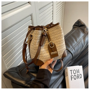 Close-up of beige straw bucket bag with brown leather trim and drawstring details