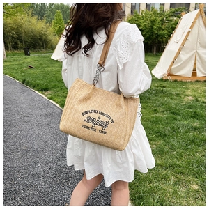 Close-up of woven straw tote bag with brown straps and chic metal chain details