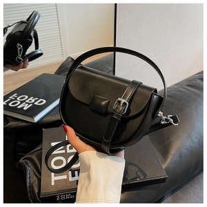 Detail of a black matte leather saddle bag with silver buckle and round top handle