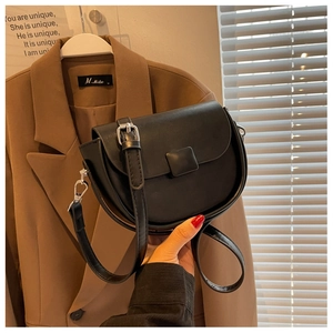 Detail of black matte leather saddle bag featuring a silver square buckle and adjustable strap