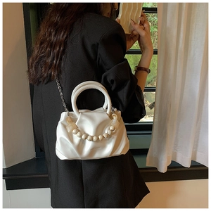 Close-up of white pleated cloud bag with elegant pearl handle and metal chain strap
