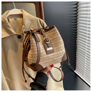 Detail of straw woven bucket bag with brown leather trim and metal clasp decoration