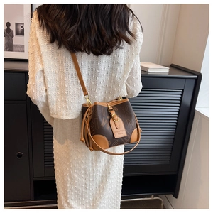Sac seau marron avec imprimé lettres porté par un mannequin en robe blanche, vue de dos