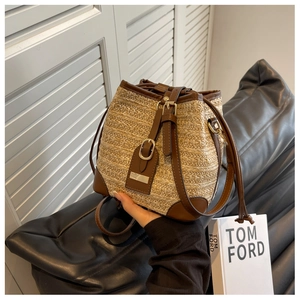 Close-up of woven straw bucket bag with brown leather trim and metallic buckle detail