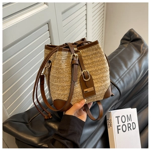 Detail of woven straw bucket bag featuring dark brown leather trim and drawstring closure