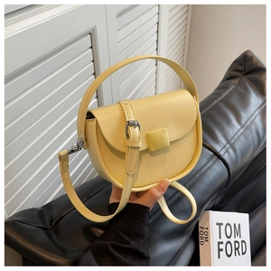 Detail view of a pale yellow saddle bag with matching handle and square metal buckle