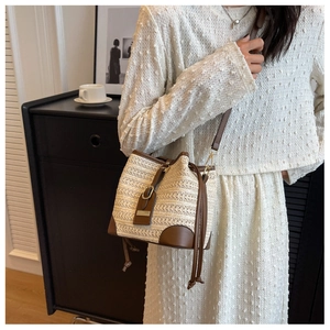 Detail of cream woven bucket bag featuring brown leather straps and drawstring closure