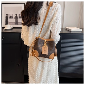 Détail d'un sac seau marron avec motif monogramme porté par un mannequin femme