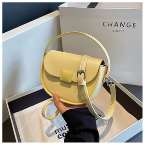 Detailed view of a light yellow saddle bag with matching buckle on a gift box background