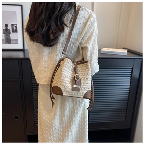 Detailed back view of a woven straw bucket bag with brown leather trim on a model