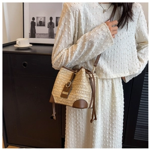 Detailed view of woven straw bucket bag with brown leather trim and drawstring closure