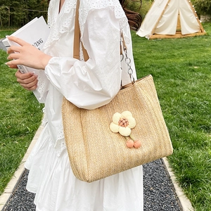 Large woven straw tote bag with floral accents and leather chain handles in outdoor setting