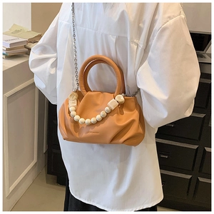 Detail of orange pleated handbag featuring a metal chain and white beaded stone strap