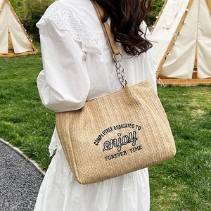 Beige woven straw tote bag with black lettering and leather chain strap for summer