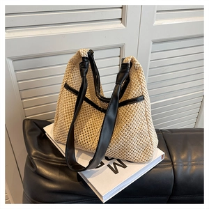 Detail of hand-woven beige straw tote bag with black leather straps on white books