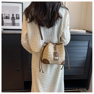 Detail of woven straw bucket bag with brown leather trim held by a model in a minimal setting