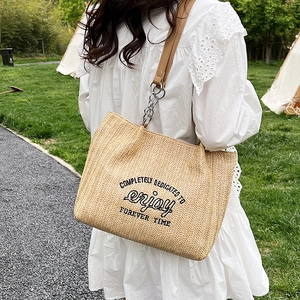 Straw woven tote bag with brown leather straps and typography design for summer beach