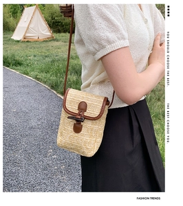 Detail of a straw woven phone bag featuring a vintage toggle closure and leather accents