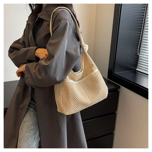 Detailed view of beige woven tote bag with hollow texture and thick shoulder straps