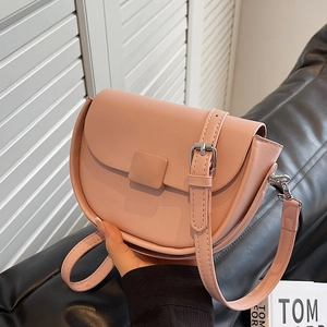 Pink minimalist half-moon saddle bag with adjustable strap on a leather sofa