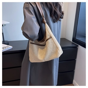 Detail of woven straw tote bag featuring brown leather trim and knotted handle detail