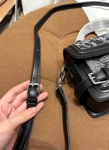 Detail of black leather crossbody bag featuring intricate white artistic embroidery and silver buckle
