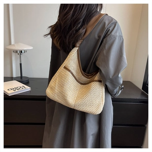 Detail of hand-woven straw tote with brown leather trim shown on a model's shoulder